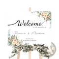 A white custom wedding welcome sign with black cursive lettering and peach pink floral watercolor accents for decor