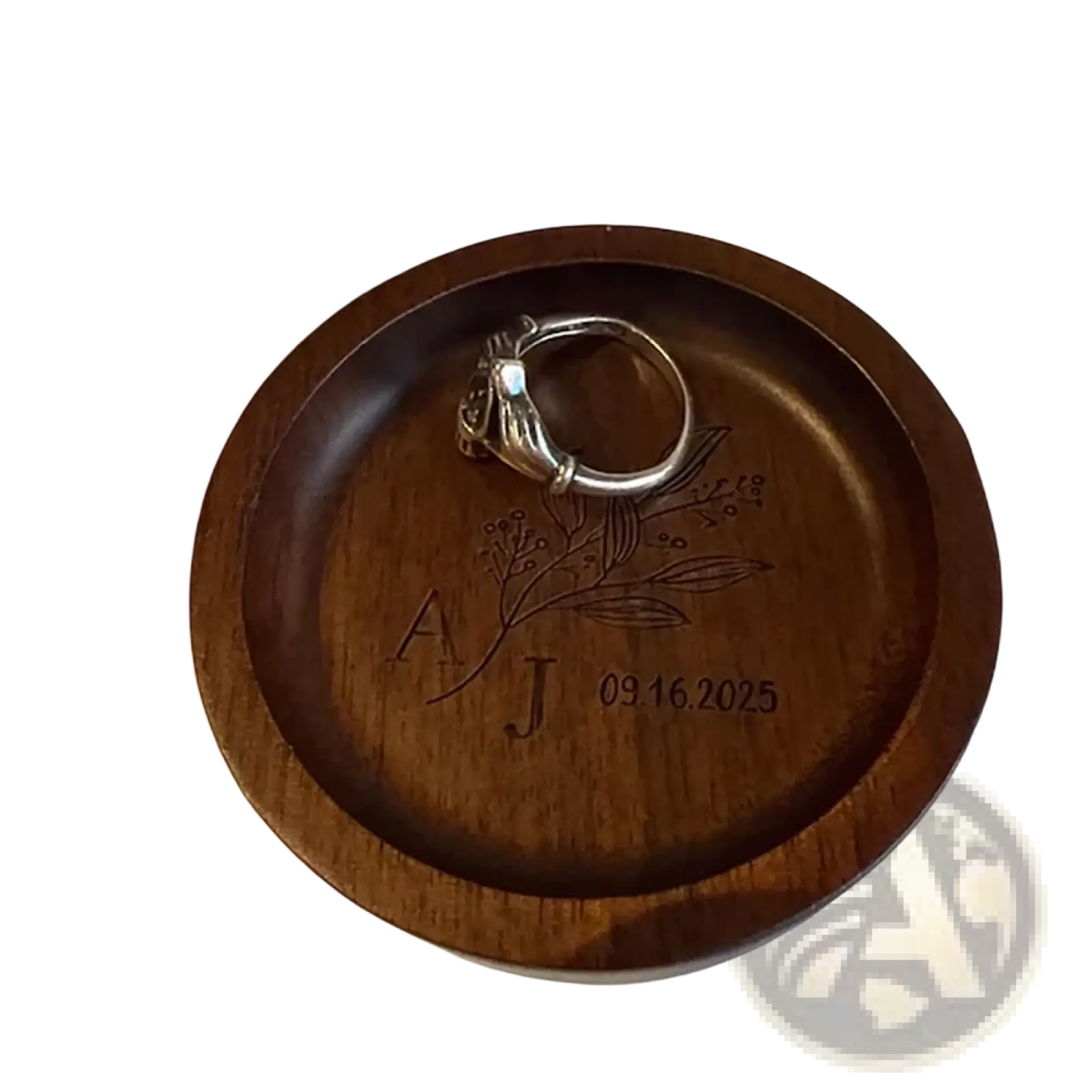 A dark brown wooden custom ring dish engraved with initials aj floral design and date 09.16.2025 for wedding rings