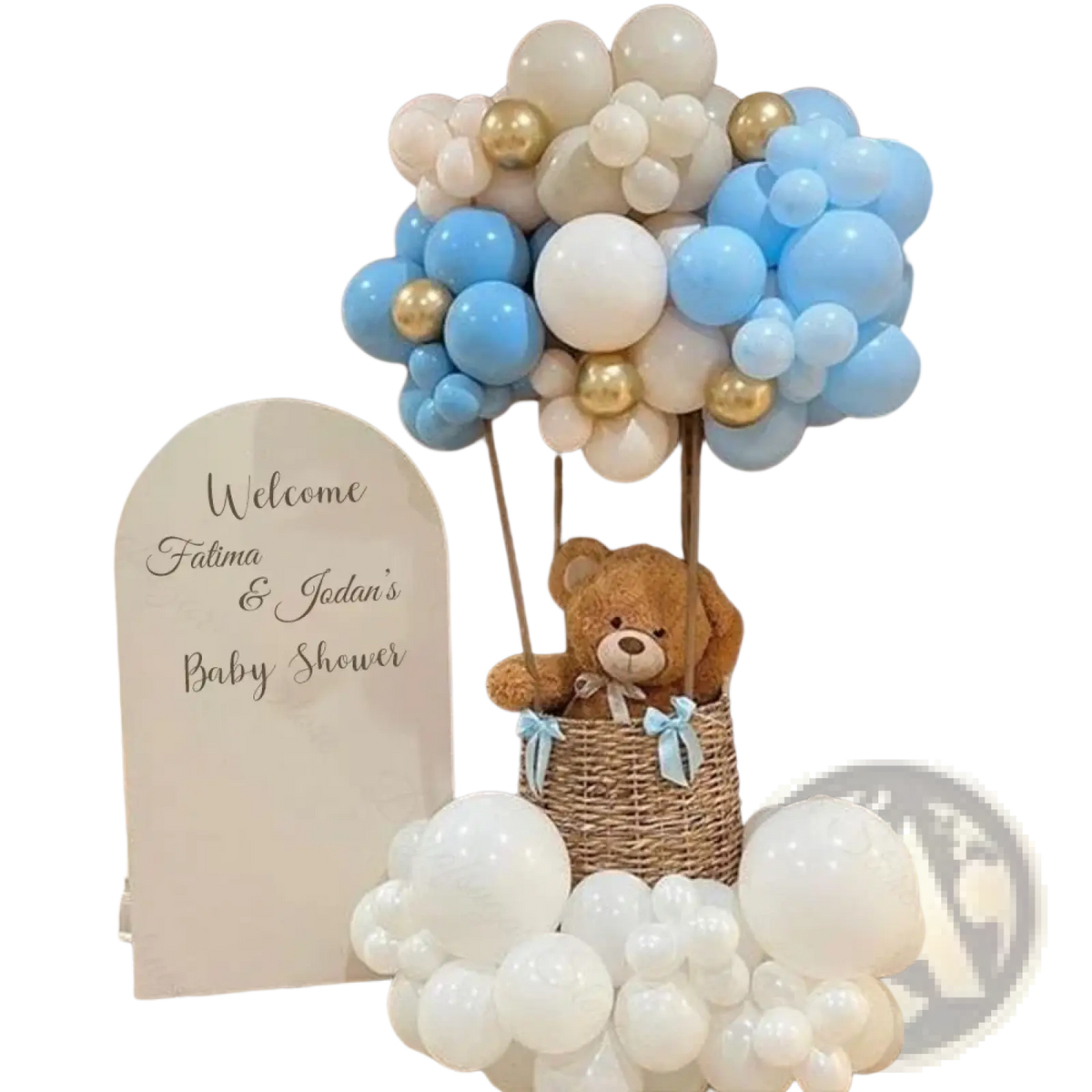 A plush brown teddy bear with a light blue ribbon in a woven wicker basket on a customized arch backdrop board for baby shower