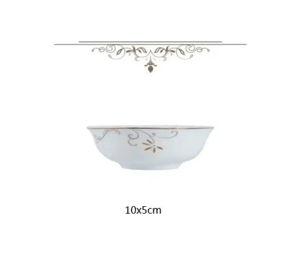 A delicate white ceramic bowl with gold leaf floral vine patterns and a metallic rim complementing a classic stainless steel flatware set
