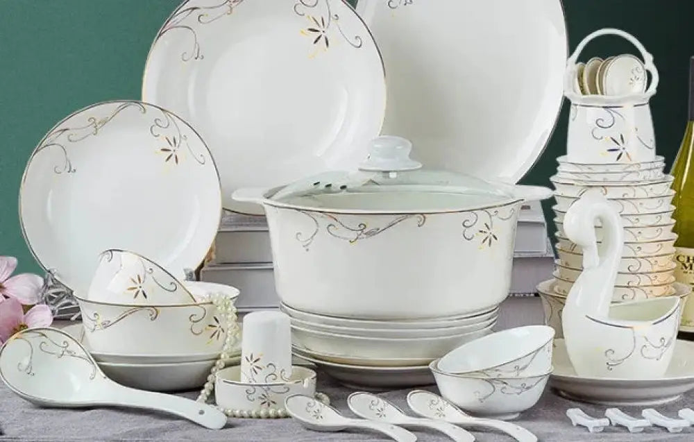 White ceramic dinnerware set with gold floral patterns and matching pot displayed alongside classic stainless steel flatware set
