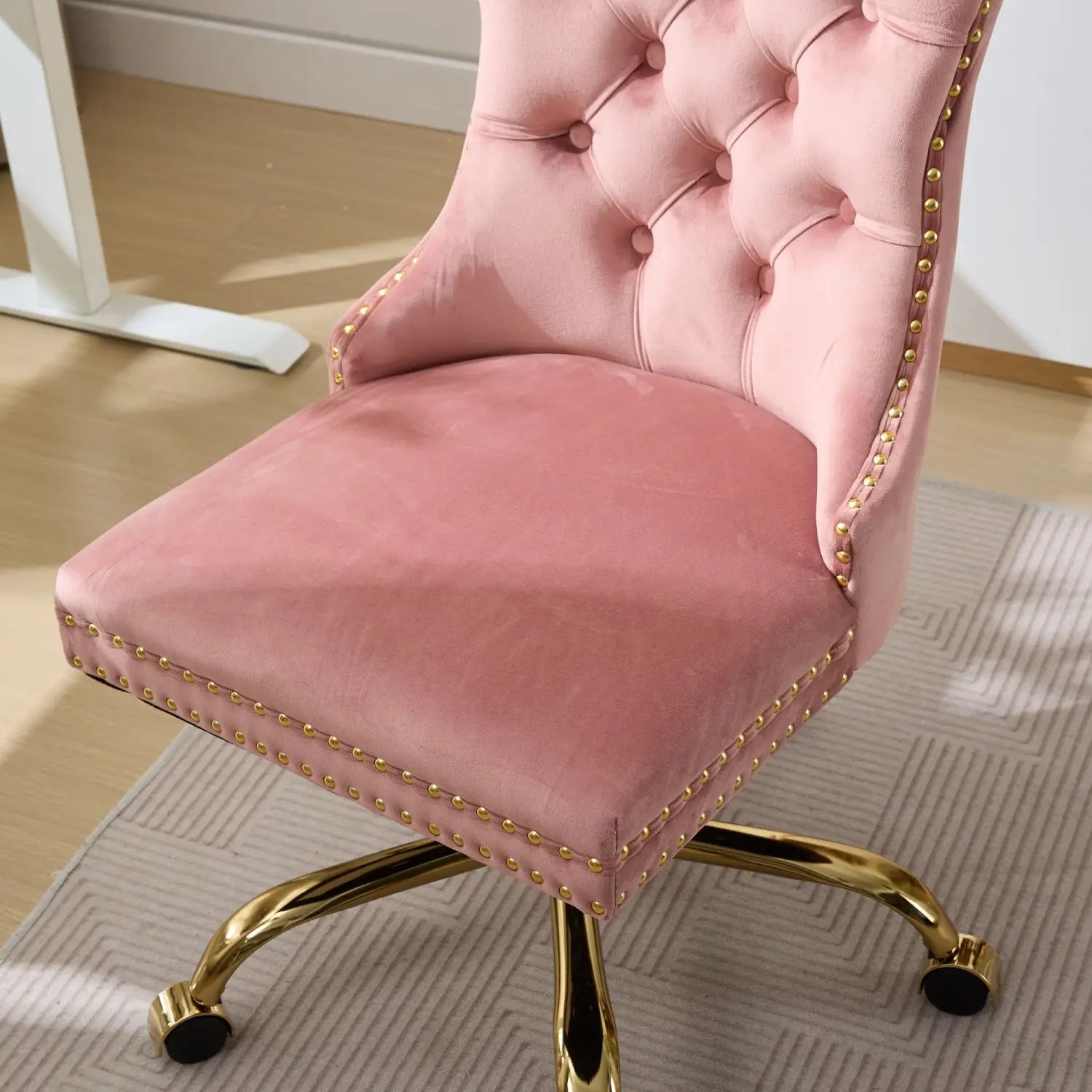 Fauteuil de bureau en velours rose poudré à capitonnage avec bordure à clous décoratifs ton doré et base en laiton poli, affiché de face