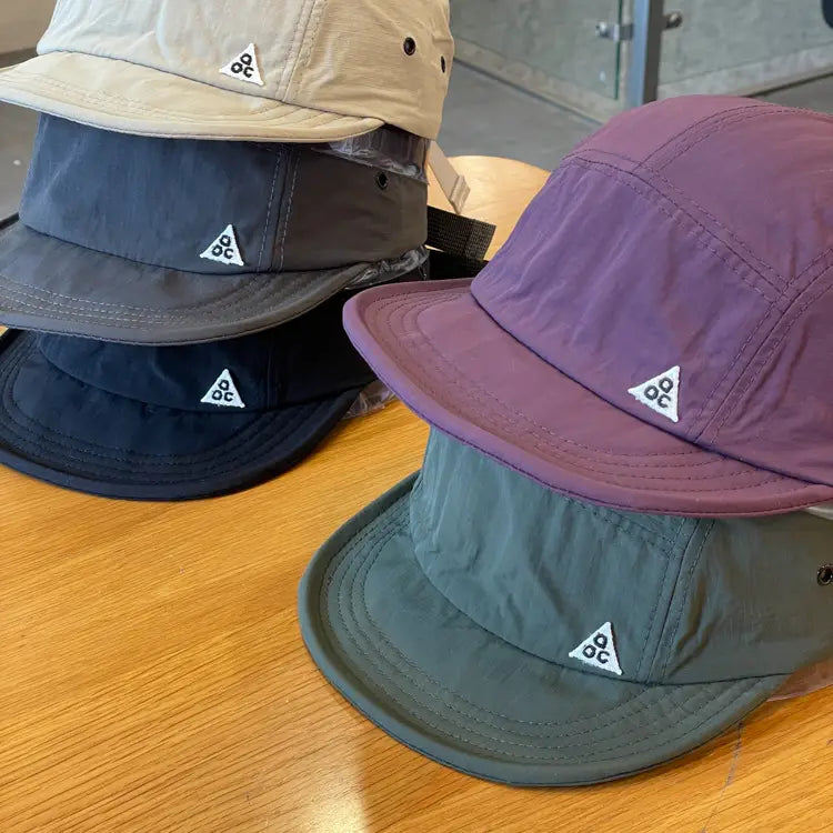 A collection of five color-blocked quick drying short brim caps in maroon made of lightweight nylon featuring a white triangular logo on the front.