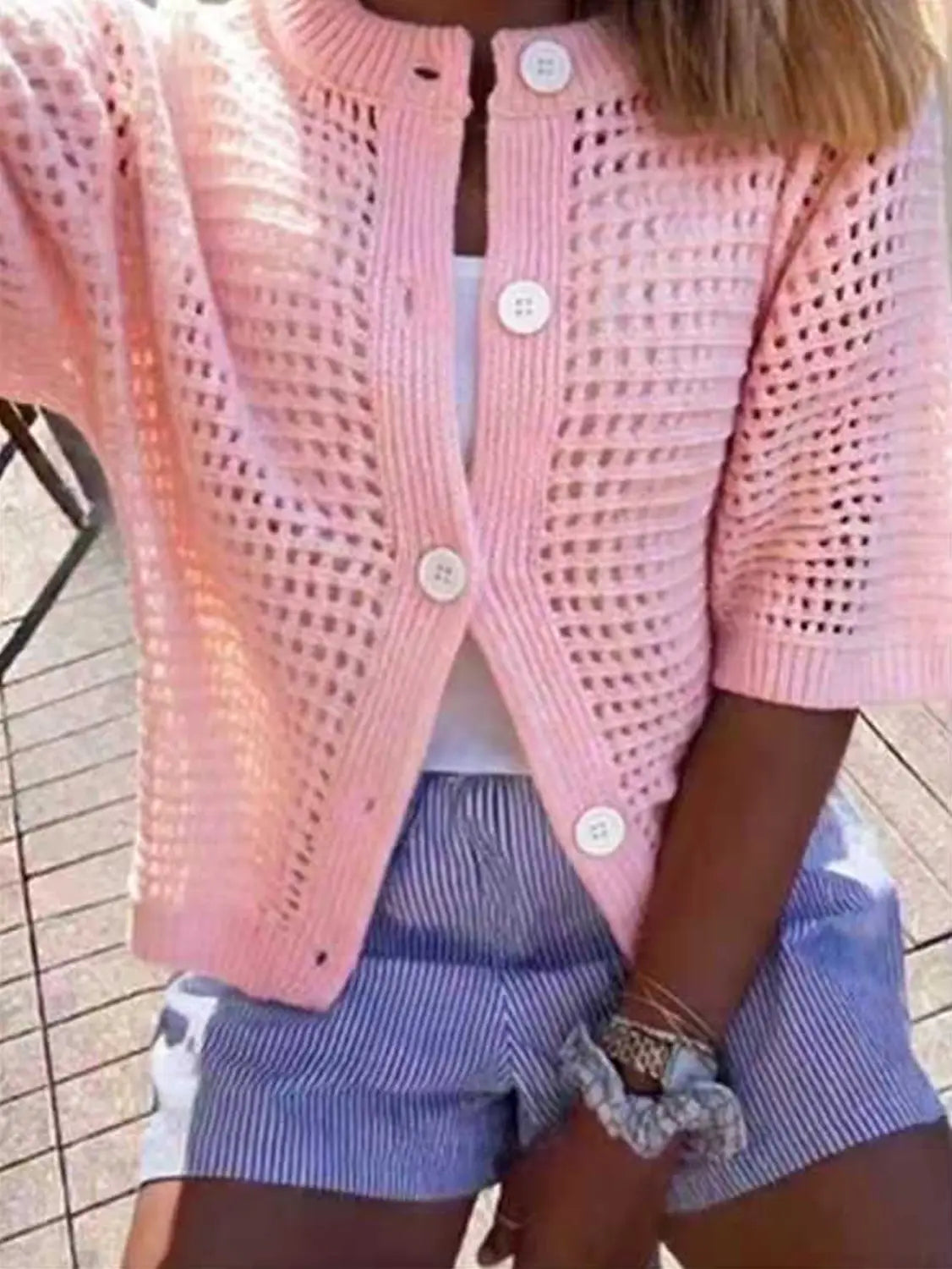 Una parte superior tipo suéter cárdigan de punto rosa suave de manga corta con calado, patrón texturizado y botones blancos.