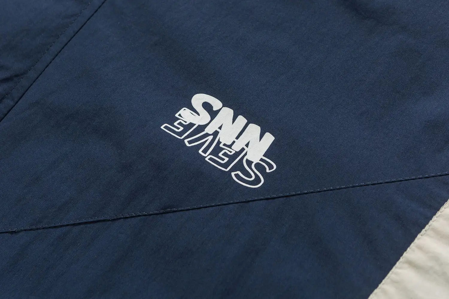 Veste coupe-vent ample bleu marine foncé avec un logo brodé blanc « snn seve » et un design à blocs de couleurs.