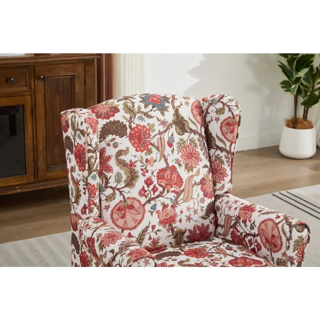 Una mullida silla tipo ala con respaldo capitoné floral, tapizada en un tejido vibrante con flores rojas llamativas, enredaderas marrones intrincadas y delicados acentos azules sobre un fondo blanco, con patas de madera retro.