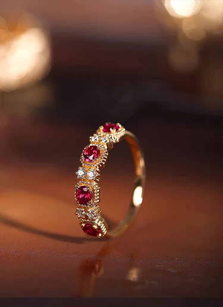 An 18k gold plated band ring featuring five vibrant pigeon blood red rubies set in ornate bezels each flanked by smaller clear diamonds.