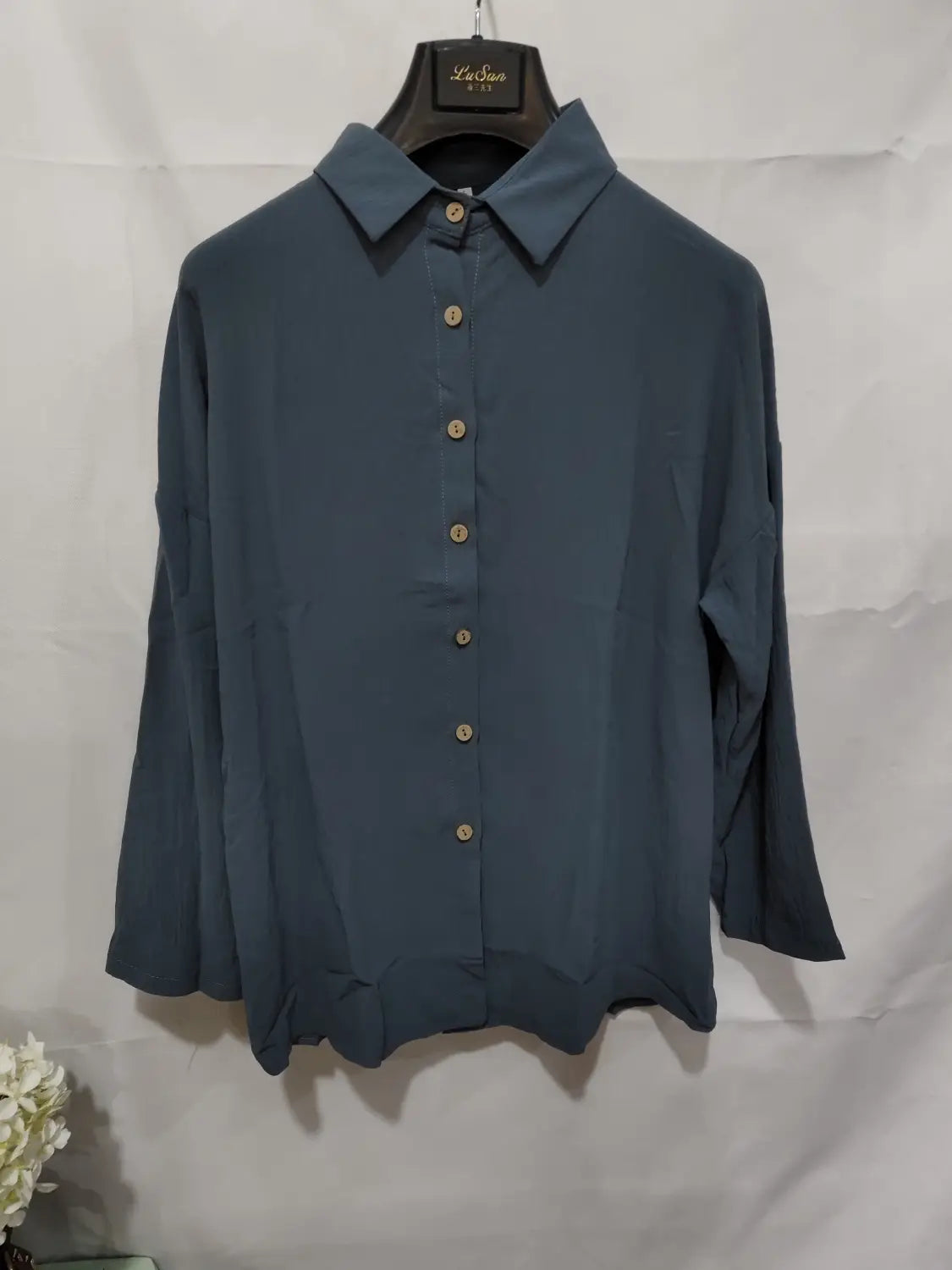A navy blue women’s relaxed pleated button up shirt with long sleeves rolled up, gold-toned buttons, and a classic collar displayed on a black hanger.