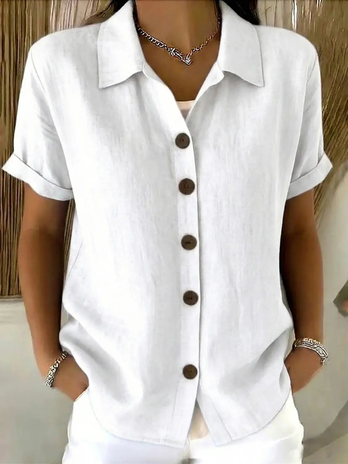 Camisa blanca abotonada de lino para mujer de manga corta, con botones marrón oscuro y puños enrollados.