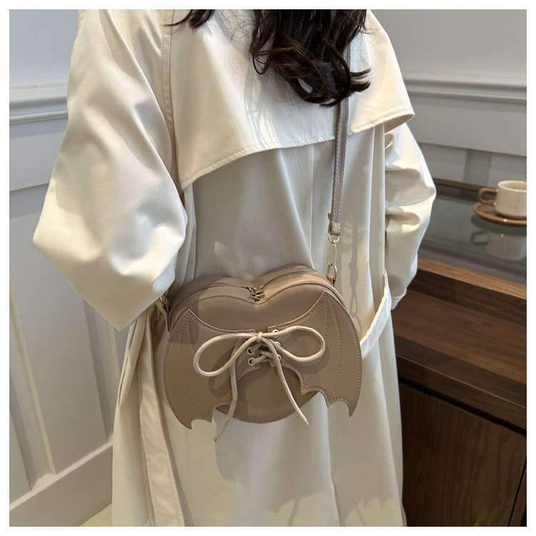 Beige bat wing heart crossbody bag with white lace-up front and gold-tone hardware.