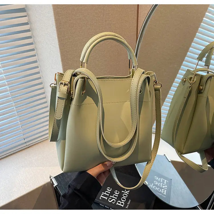 Minimalist leather bucket bag in olive green featuring dual top handles and a detachable shoulder strap.