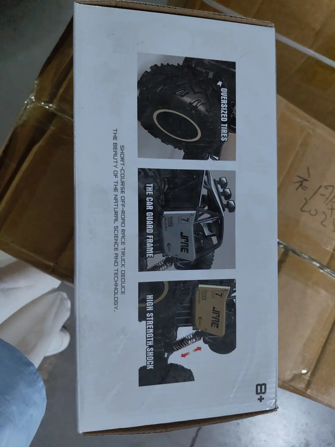 Caja de cartón blanca para el juguete de camioneta teledirigida RC todoterreno 4WD de alta velocidad de la marca Jfre, con imágenes de neumáticos de gran tamaño y componentes de amortiguación de alta resistencia.