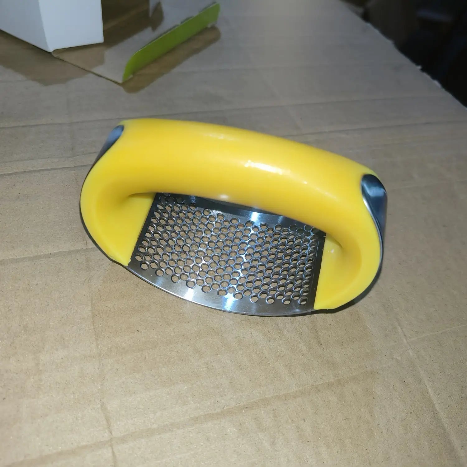 Presse-ail en plastique jaune à surface de râpage en acier inoxydable, pour un hachage manuel ergonomique.