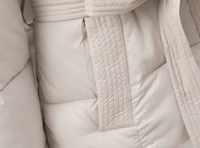 A cream-colored quilted hooded winter puffer coat with stitched belt detail designed for women.