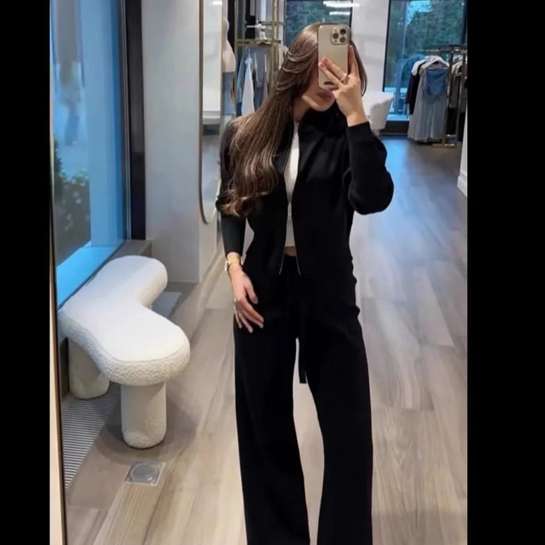 Black knit zip-up cardigan with high collar and long sleeves worn over a white top as part of a women’s knit zip up cardigan and wide leg pant set.