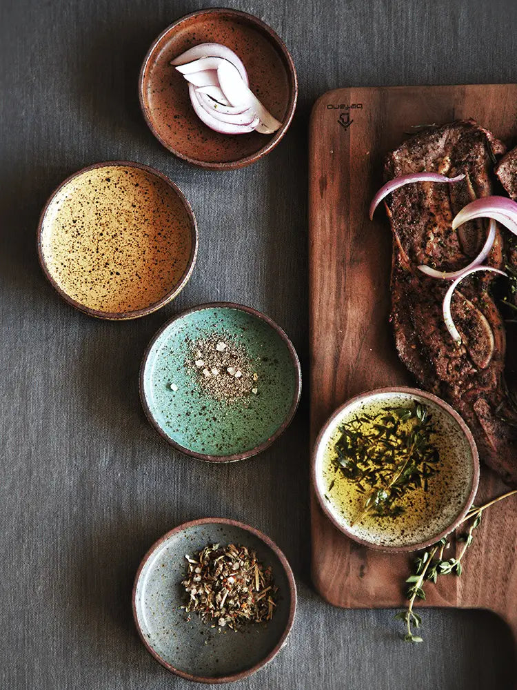 Set of five rustic ceramic sauce dishes with speckled glaze and handcrafted rims in earthy tones designed as Japanese dipping bowls.