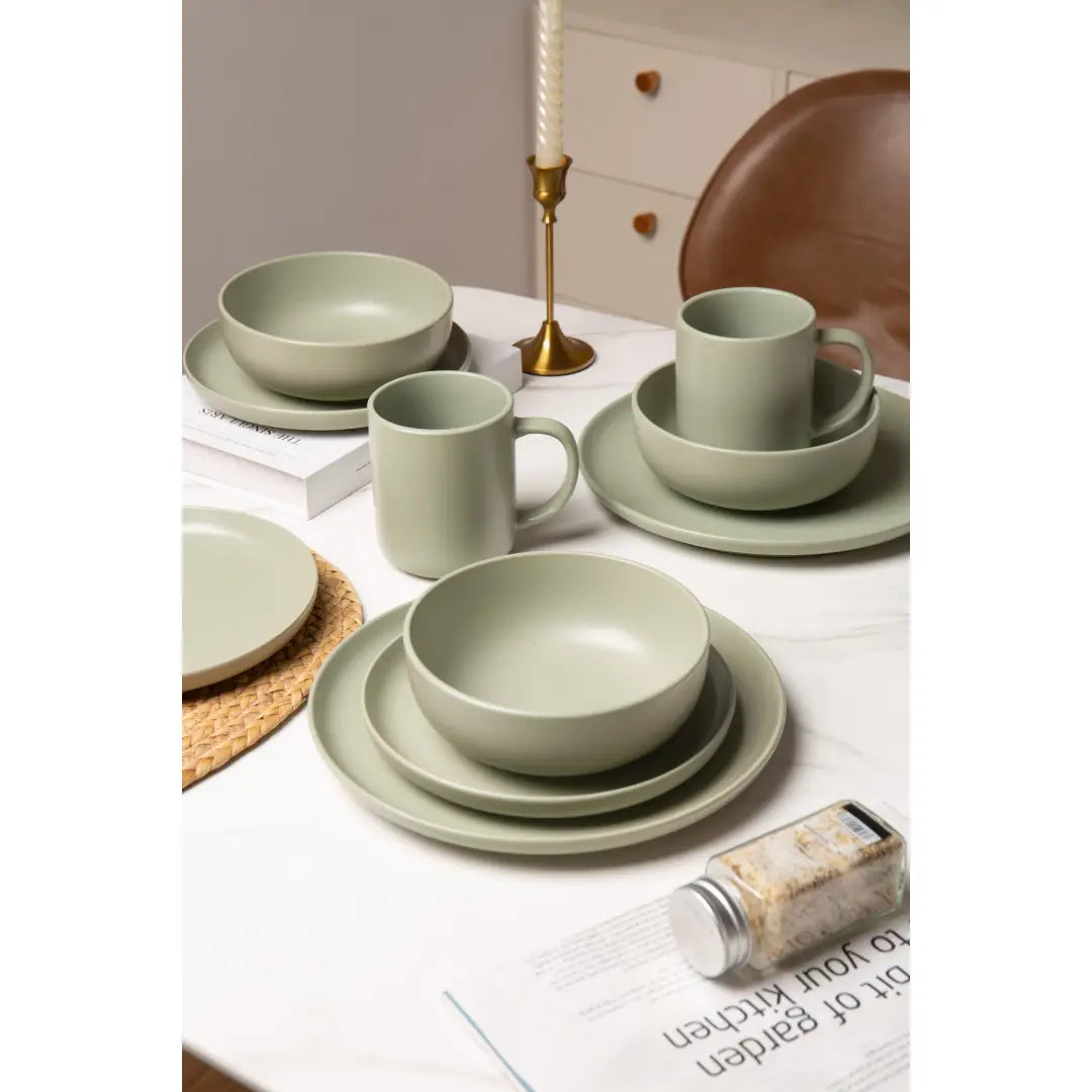 ensemble de vaisselle en grès cérame vert sauge mat, comprenant des bols, des assiettes et des tasses, disposés sur une table pour trois personnes.
