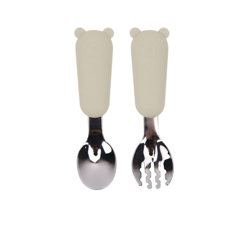 Manches en silicone de forme d’ours couleur crème sur un ensemble de couverts pour cuillère et fourchette pour bébé en acier inoxydable brillant.