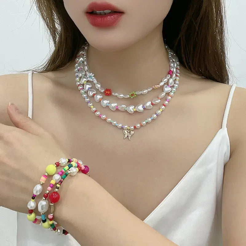 Layered gold butterfly and pearl jewelry set for women featuring a layered pearl and bead choker necklace with heart-shaped charms and a butterfly pendant.