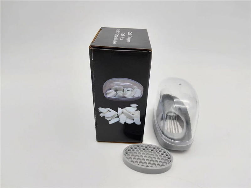 Presse-ail en plastique gris avec lames en acier inoxydable, couvercle transparent et accessoire assorti pour râper de forme ovale en gris.