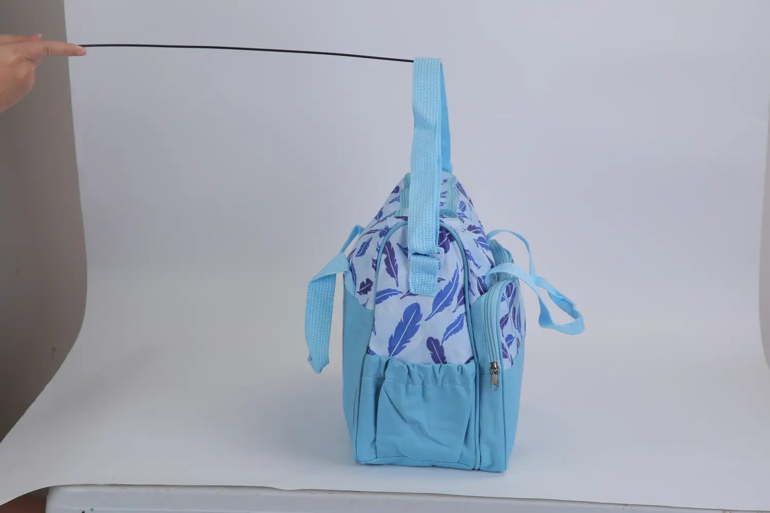 Light blue baby diaper bag with white and purple feather pattern featuring multiple zippers and adjustable straps from a 5 piece patterned baby diaper bag set with travel accessories.