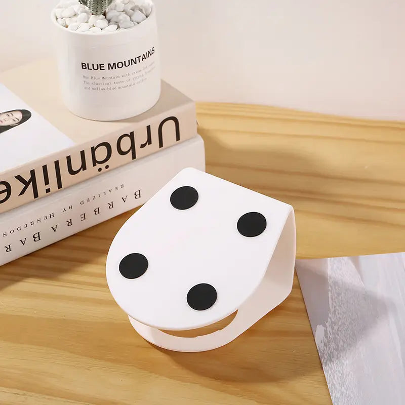 white plastic dice-shaped phone stand with black circular dots shown alongside an orthopedic cat ear pet bowl designed for slanted neck protection.