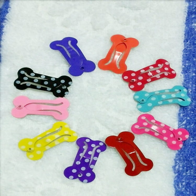 A set of colorful bone-shaped dog hair clips featuring solid and polka-dotted shiny plastic surfaces and metal barrettes for pets.
