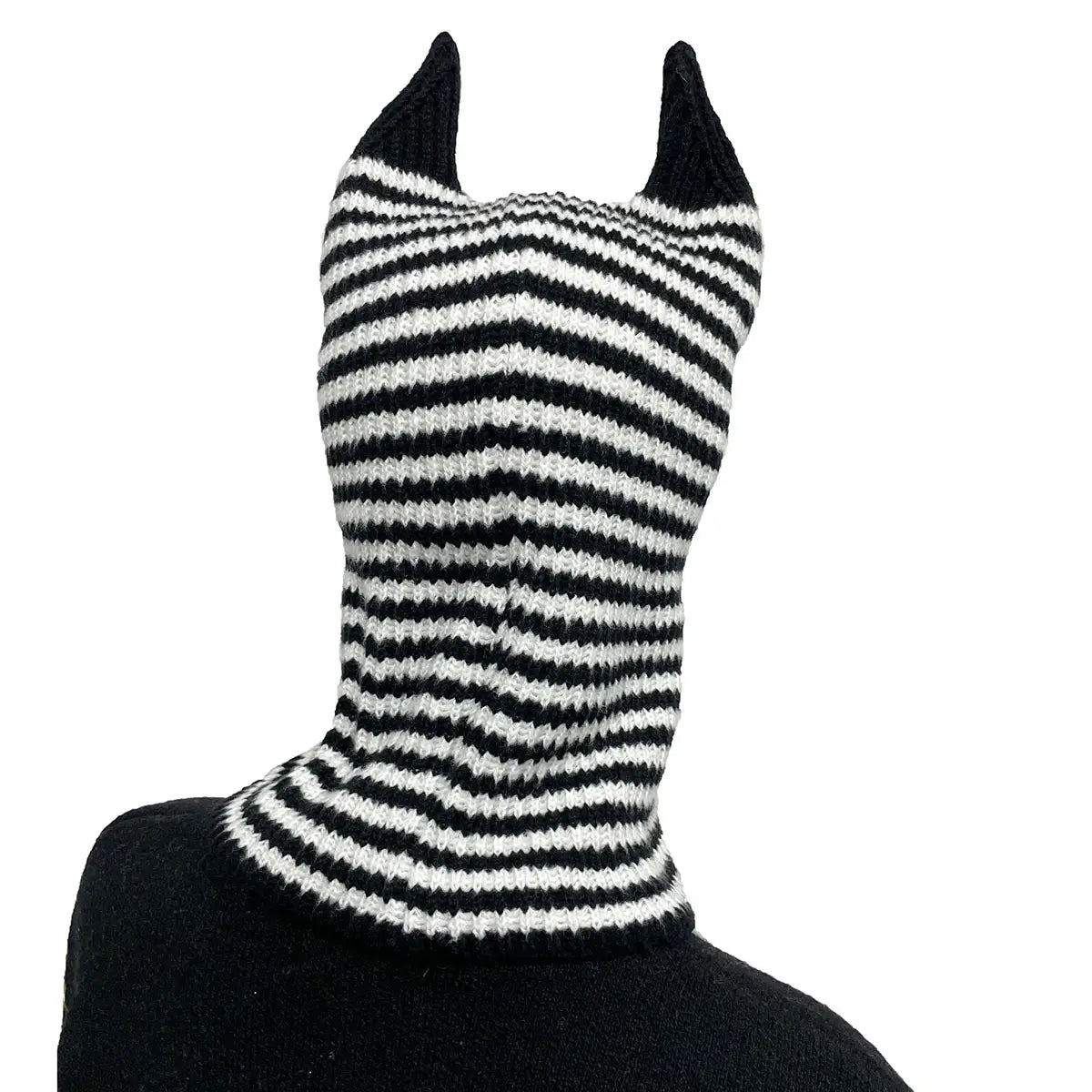 Bonnet hivernal de type cagoule tricoté à rayures noir et blanc, avec des protubérances pointues en forme d’oreilles.