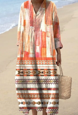 A flowing patchwork-style women’s abstract v neck patterned maxi dress in warm tones of orange peach and cream with intricate geometric patterns along the hem.