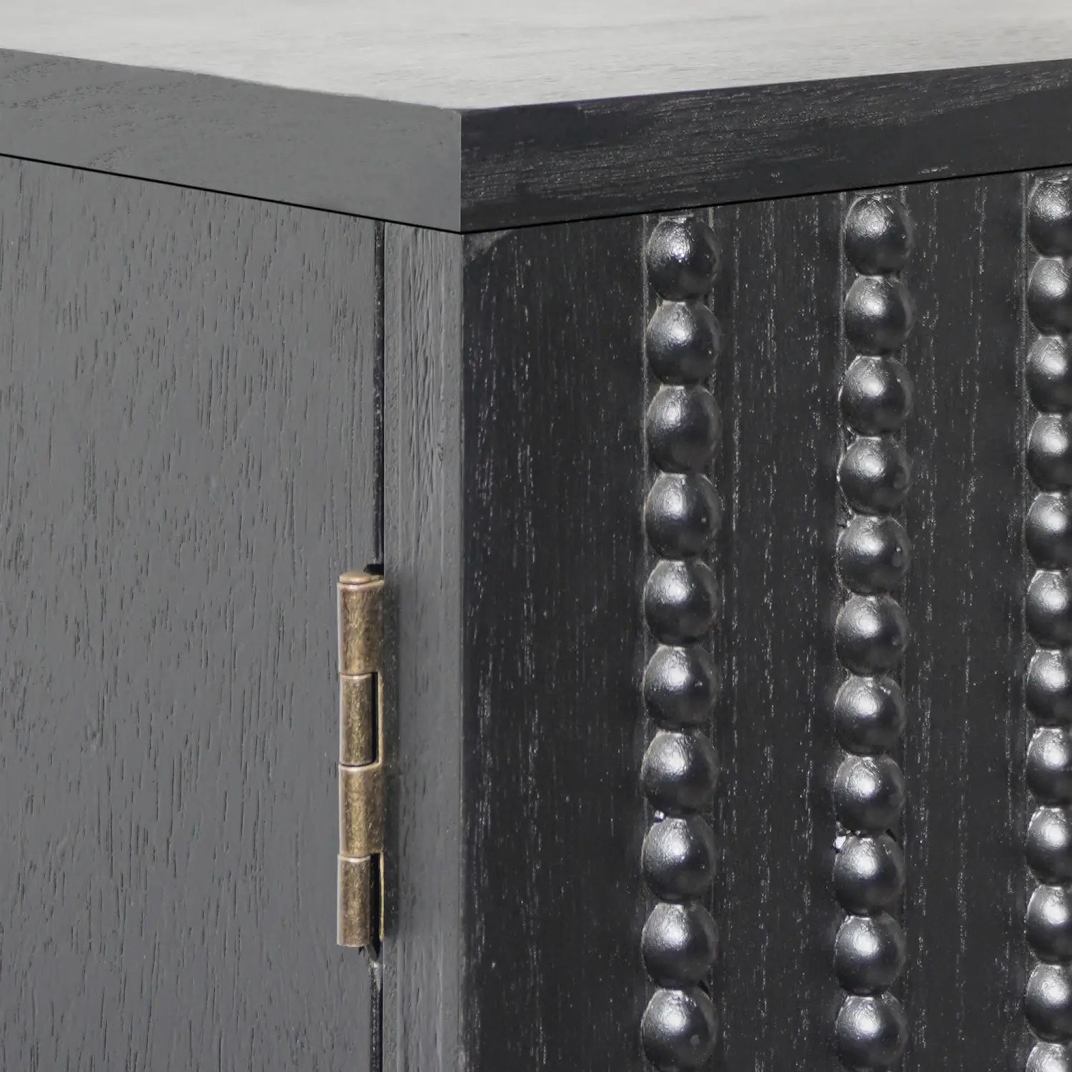 black storage cabinet with arched beaded door featuring vertical rows of metallic beaded accents and a brass hinge on black wood material.