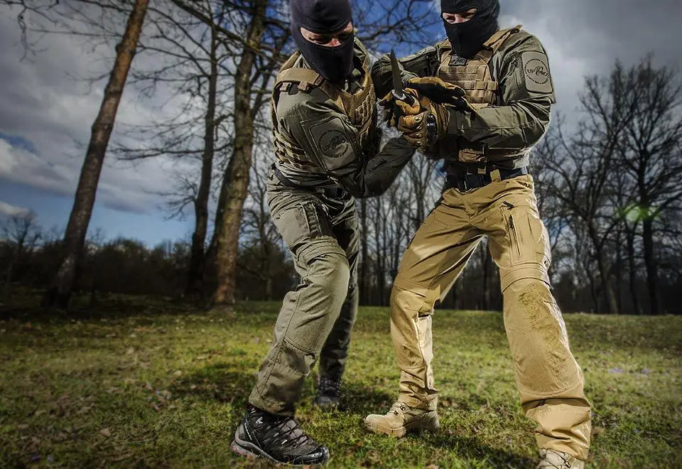Deux opérateurs tactiques portant des pantalons tactiques P40 pour hommes à motif camouflage olive et beige, multi-poches, avec des cagoules noires, engagés dans des manœuvres de combat en combat rapproché en extérieur.