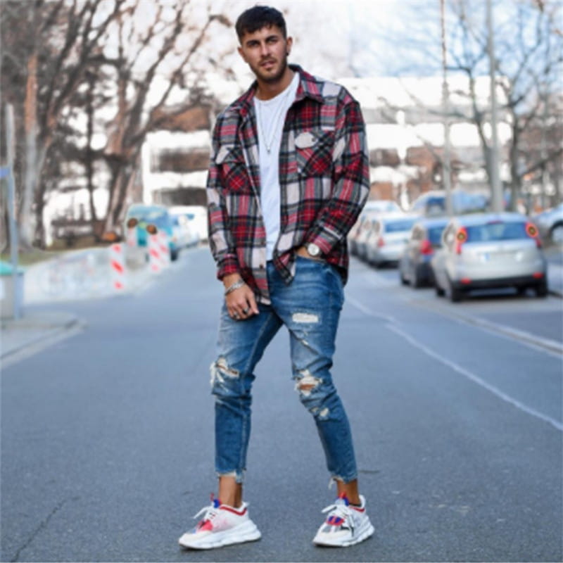 Men’s distressed blue denim ripped knee jeans paired with a red and black plaid flannel shirt featuring a white buttoned front.