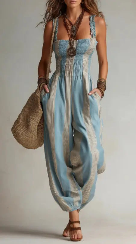 A flowing light blue and beige striped boho square neck harem jumpsuit with a smocked bodice wide-leg pants and adjustable shoulder straps.