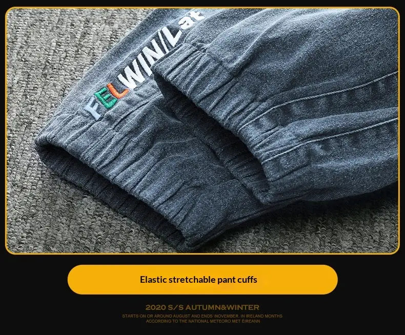 Men’s relaxed fit dark gray denim joggers with elastic stretchable cuffs and a colorful embroidered logo on the waistband and drawstring waist.