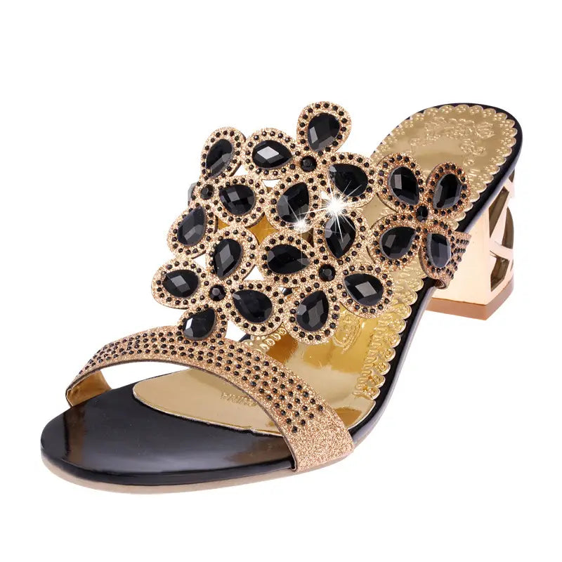 Black and gold rhinestone high heel slide-on sandal embellished with floral design of black teardrop-shaped stones set in gold-toned metal.