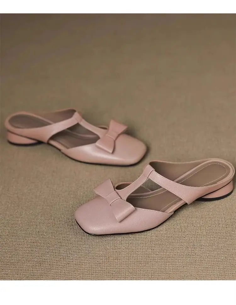 Pair of light pink leather closed toe mule flats for women featuring a bow detail on the strap.
