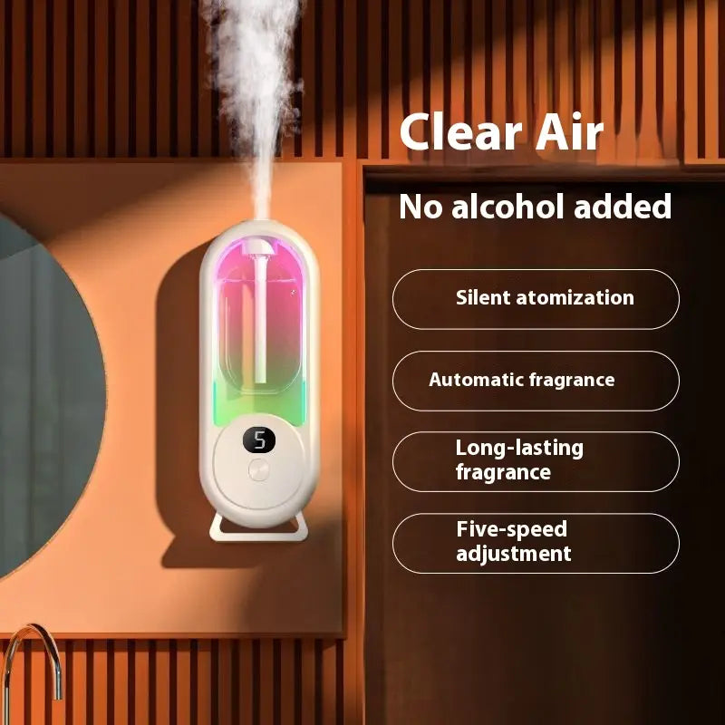 A sleek white and translucent digital aroma diffuser automatic air freshener lamp with a glowing rainbow interior emitting mist from its top.