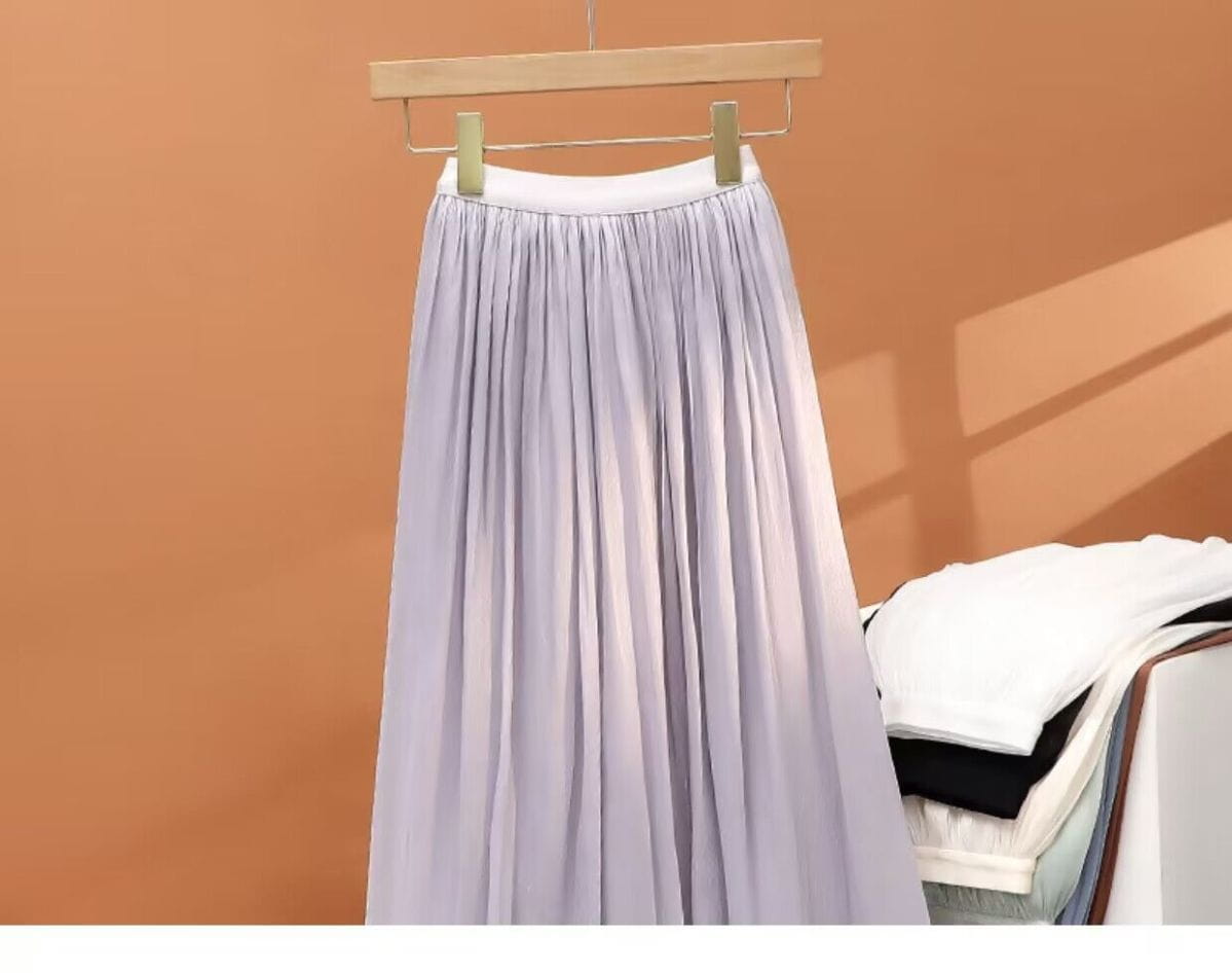 Ein fließender lavendelfarbener irrisierender Chiffon-Faltenrock mit weißem Bund, der an einem Holzkleiderbügel hängt.
