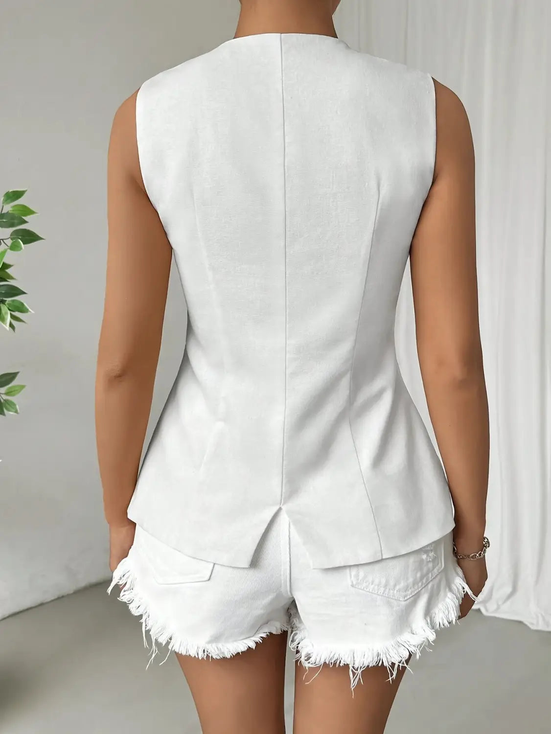 Veste sans manches à volants peplum blanche, avec dos structuré, associée à un short en jean blanc assorti à bords effilochés.