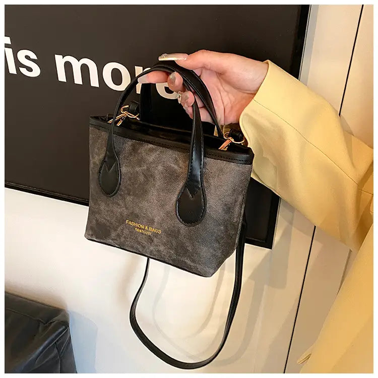 A stylish gray and black patterned retro bucket bag featuring textured canvas, contrasting black leather handles, a detachable strap, and gold-tone hardware.