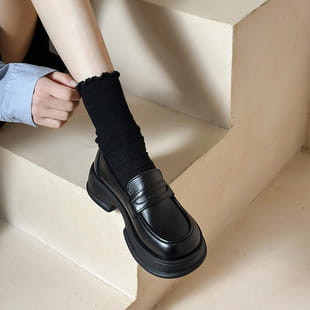 Black leather loafers with a thick chunky sole and classic slip-on design contrasting with the product titled brown leather loafers with gold buckle detail.