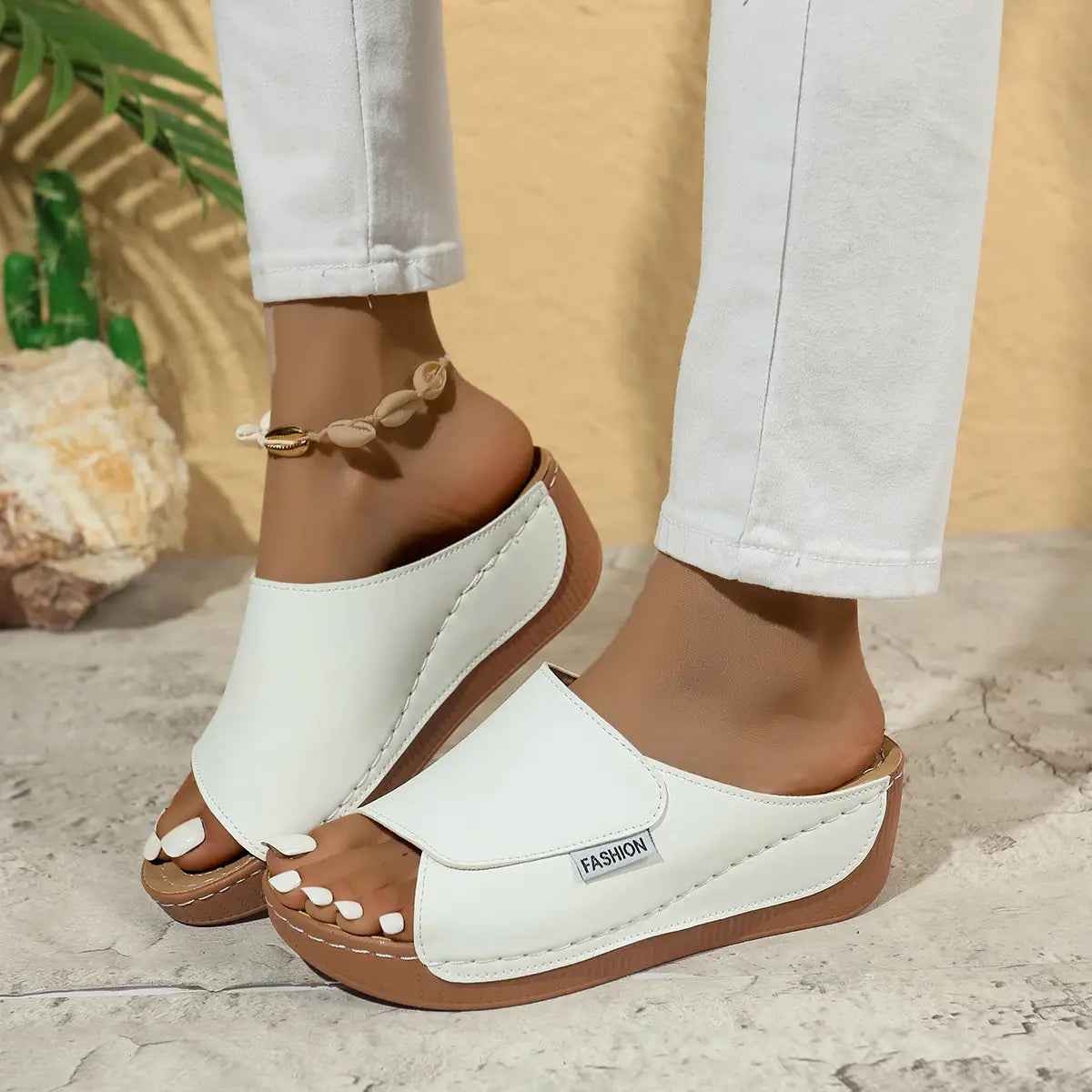 Sandales d’été à plateforme compensée à bride glissante pour femmes en cuir blanc, avec une semelle marron et un étiquetage de mode sur le côté.