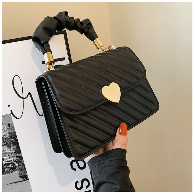 Black quilted crossbody handbag with gold heart clasp and ruched black handle designed for stylish everyday use.