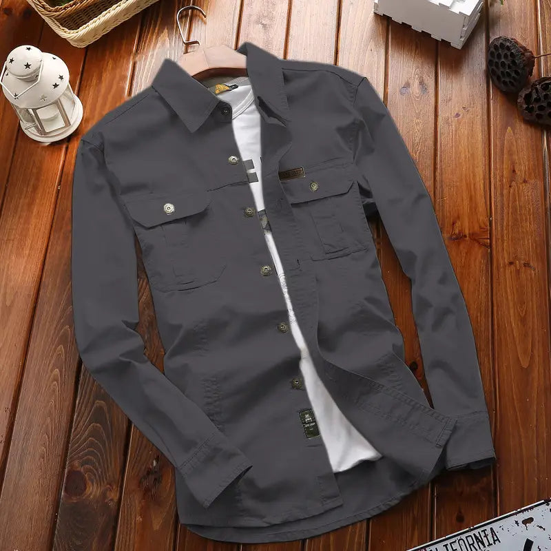 Chemise d’homme d’extérieur à manches longues boutonnée unie gris foncé, avec deux poches de poitrine et un t-shirt blanc visible en dessous.