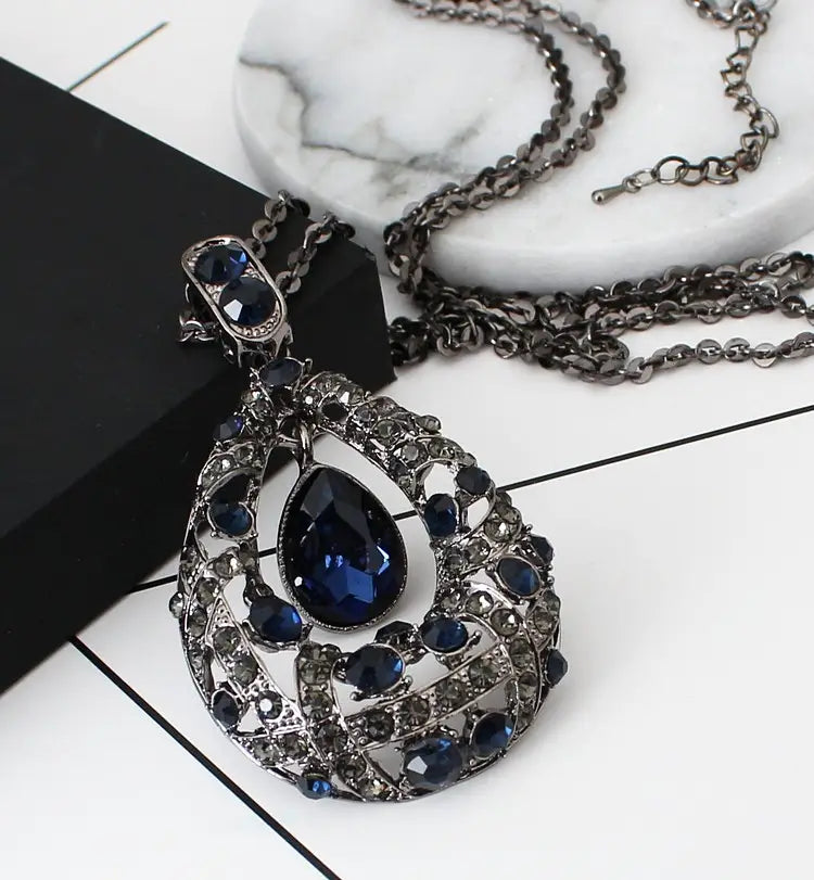 A dark blue teardrop filigree pendant necklace with intricate silver-toned metalwork and embedded crystals on a Korean style sweater chain.