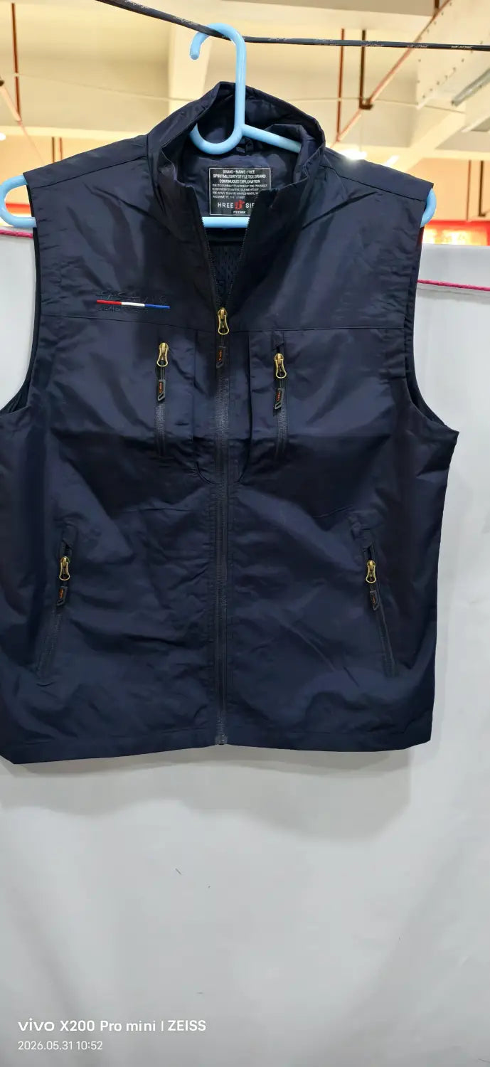 Chaleco utilitario con capucha y múltiples bolsillos para hombre en nailon azul marino oscuro, con cremalleras de tono dorado y un pequeño logotipo bordado en el lado izquierdo del pecho.
