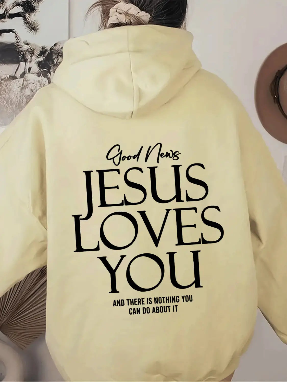 a pale yellow oversized streetwear hoodie with a hood and kangaroo pocket showing the back side with bold black text reading jesus loves you across it