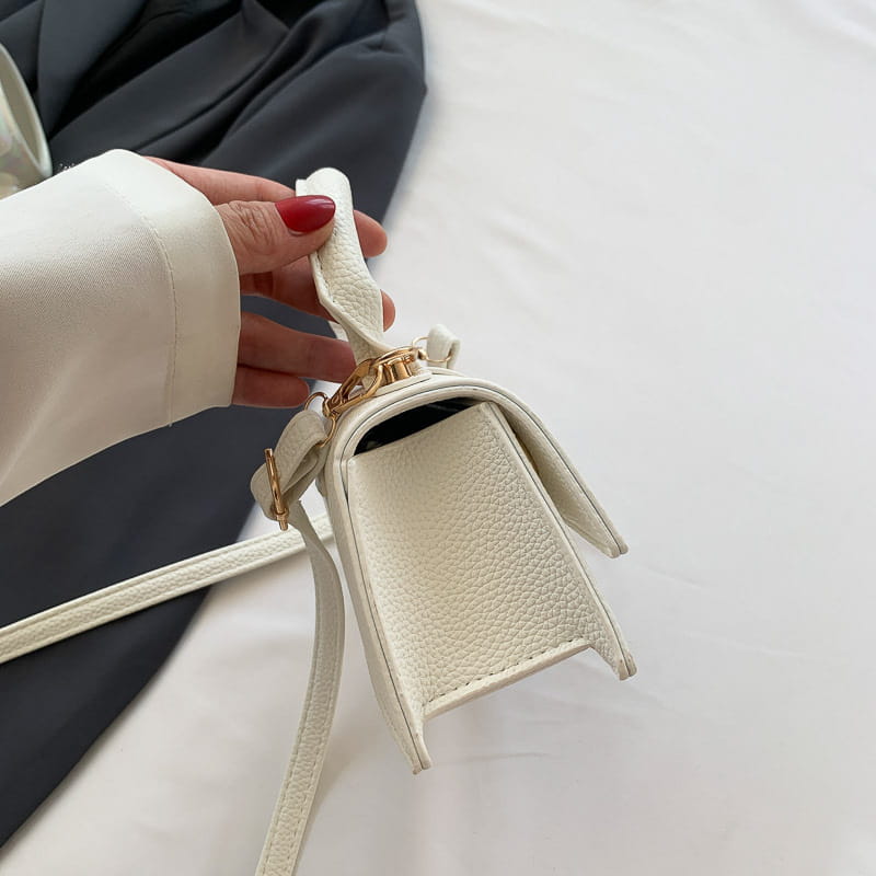 Eine weiße, strukturierte Mini-Crossbody-Tasche aus Lederoptik mit goldfarbenen Beschlägen und einem abnehmbaren Riemen, ausgelegt als Ketten-Umhängetasche Mini aus Kunstleder.