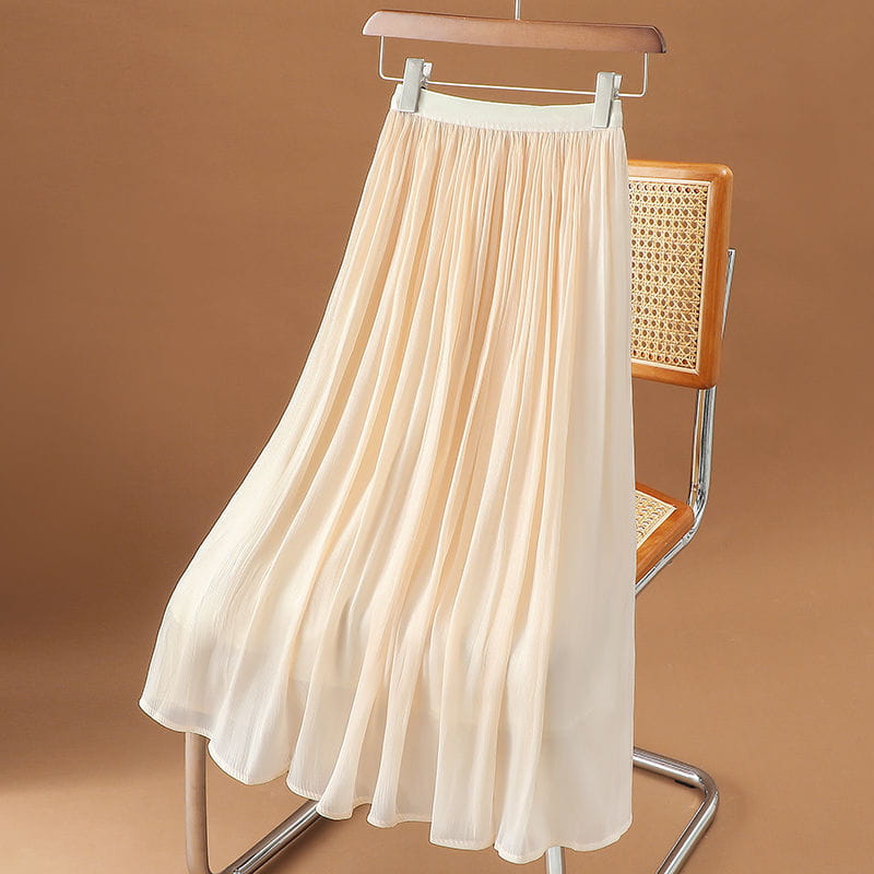 Ein cremefarbener irrisierender Chiffon-Faltenrock im Midi-Format aus weichem, leichtem Gewebe, der elegant an einem Holzkleiderbügel hängt.