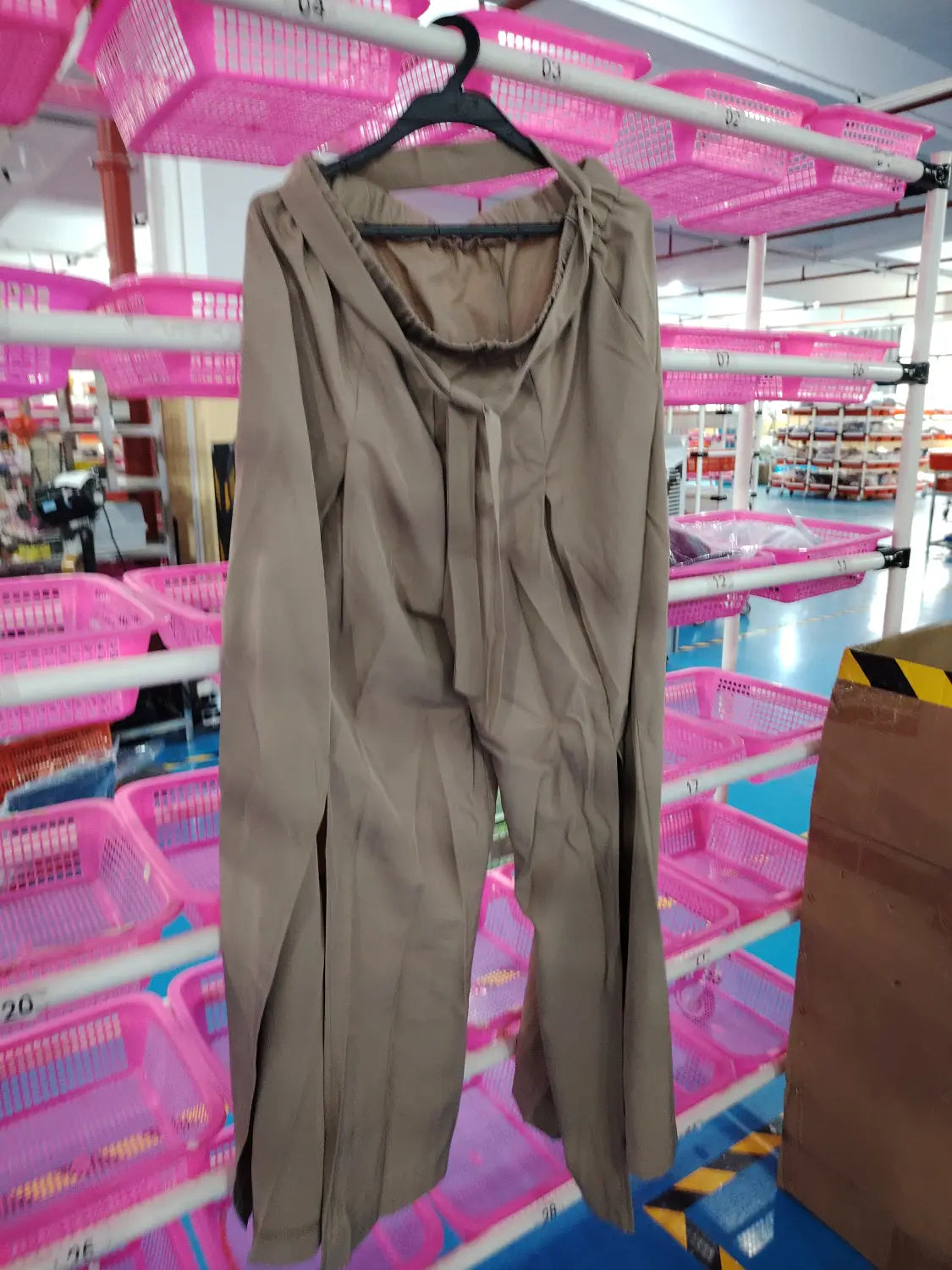 Haut beige à manches longues avec encolure drapée et fente avant, suspendu sur un cintre noir, associé à un pantalon ample décontracté à taille haute.